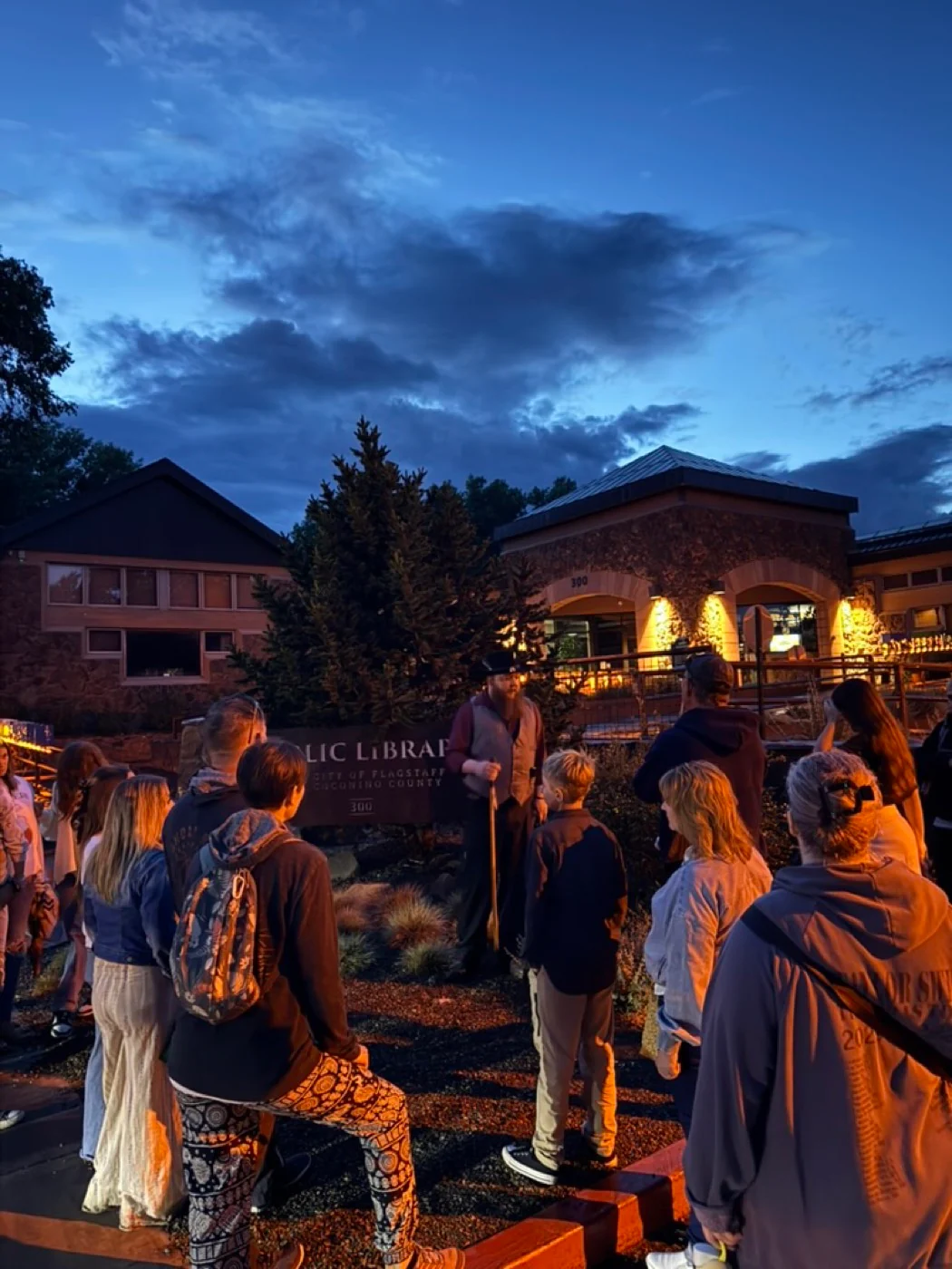 A costumed guide telling a story beside the Flagstaff library sign at night