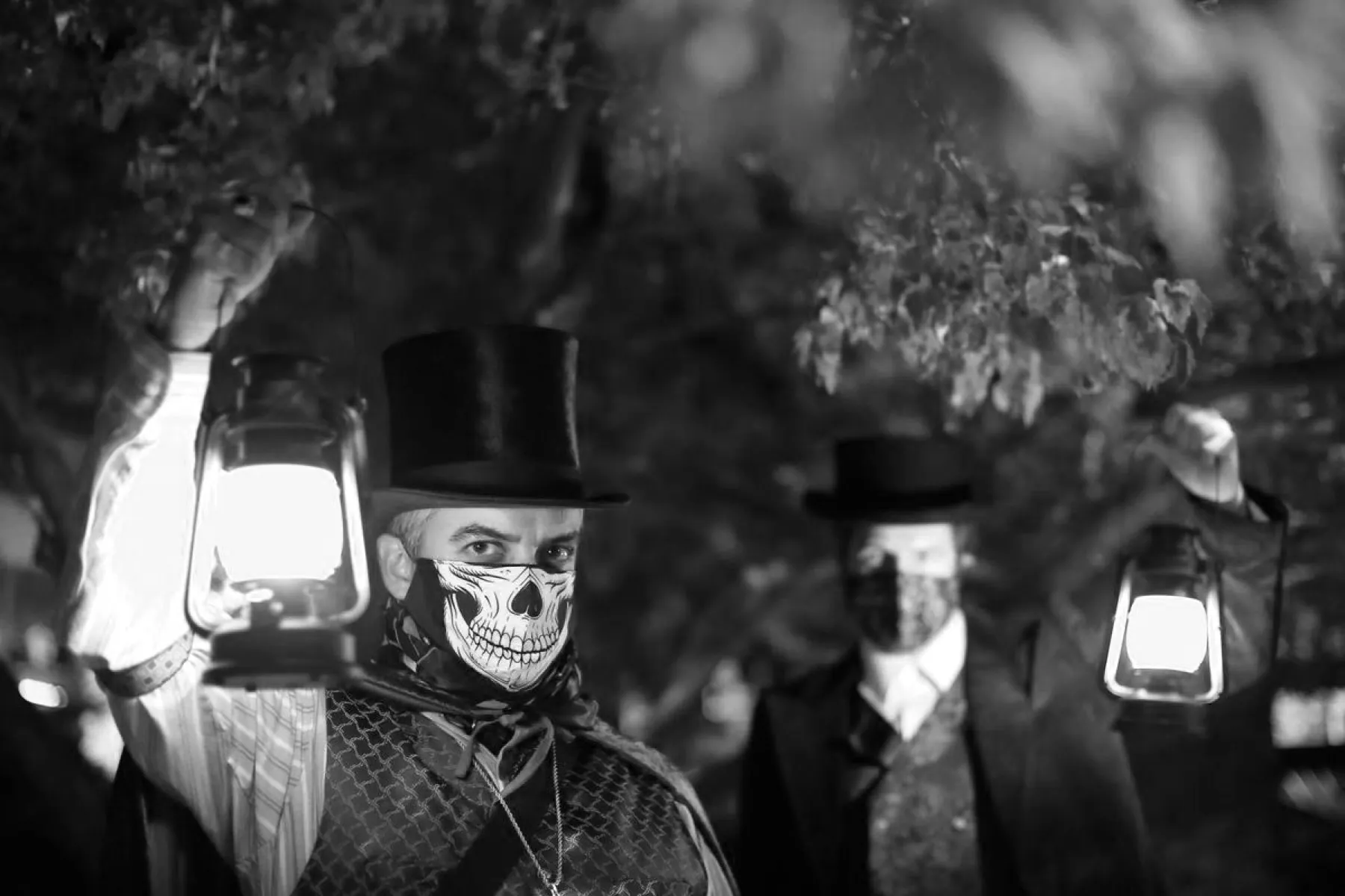 Two costumed Freaky Foot Tours guides in top hats and skull masks holding glowing lanterns on a dark Flagstaff street